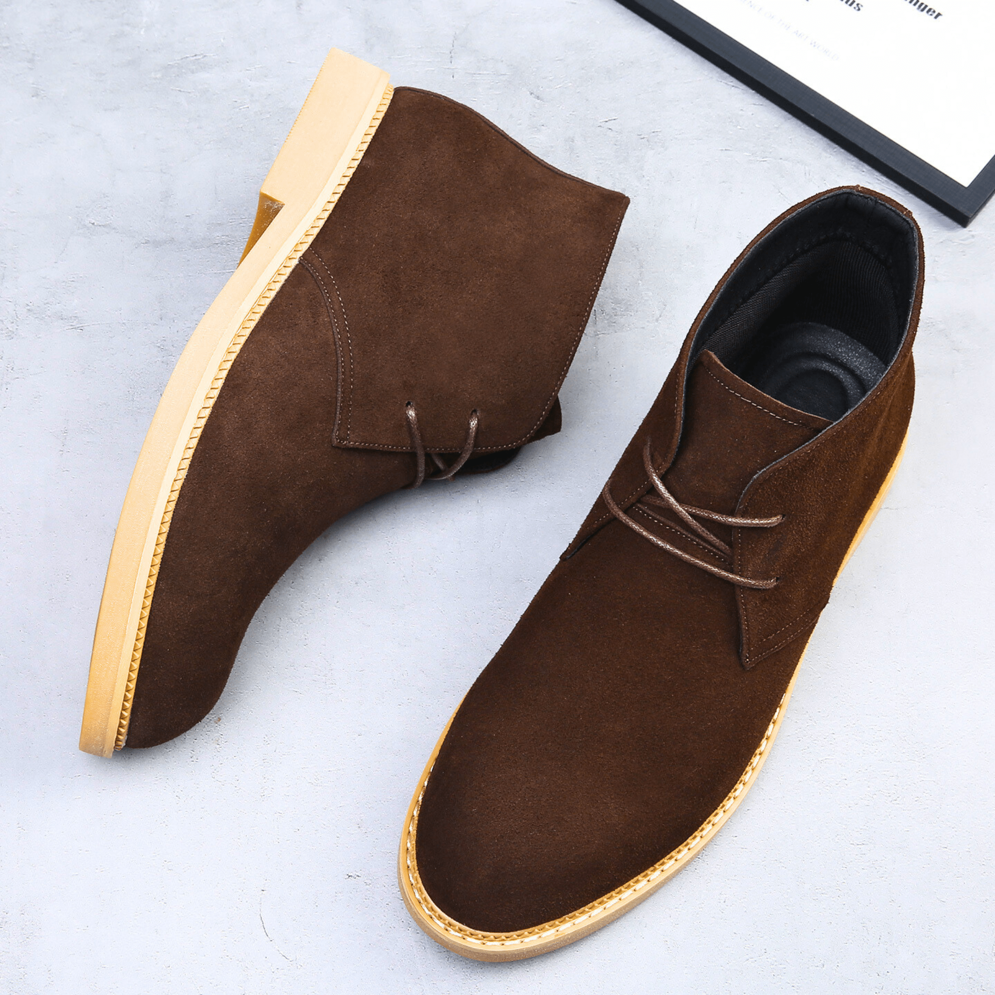 Dark brown suede-look desert boots with a plain toe, two-eyelet lacing, and a light-colored stacked sole on a grey surface.