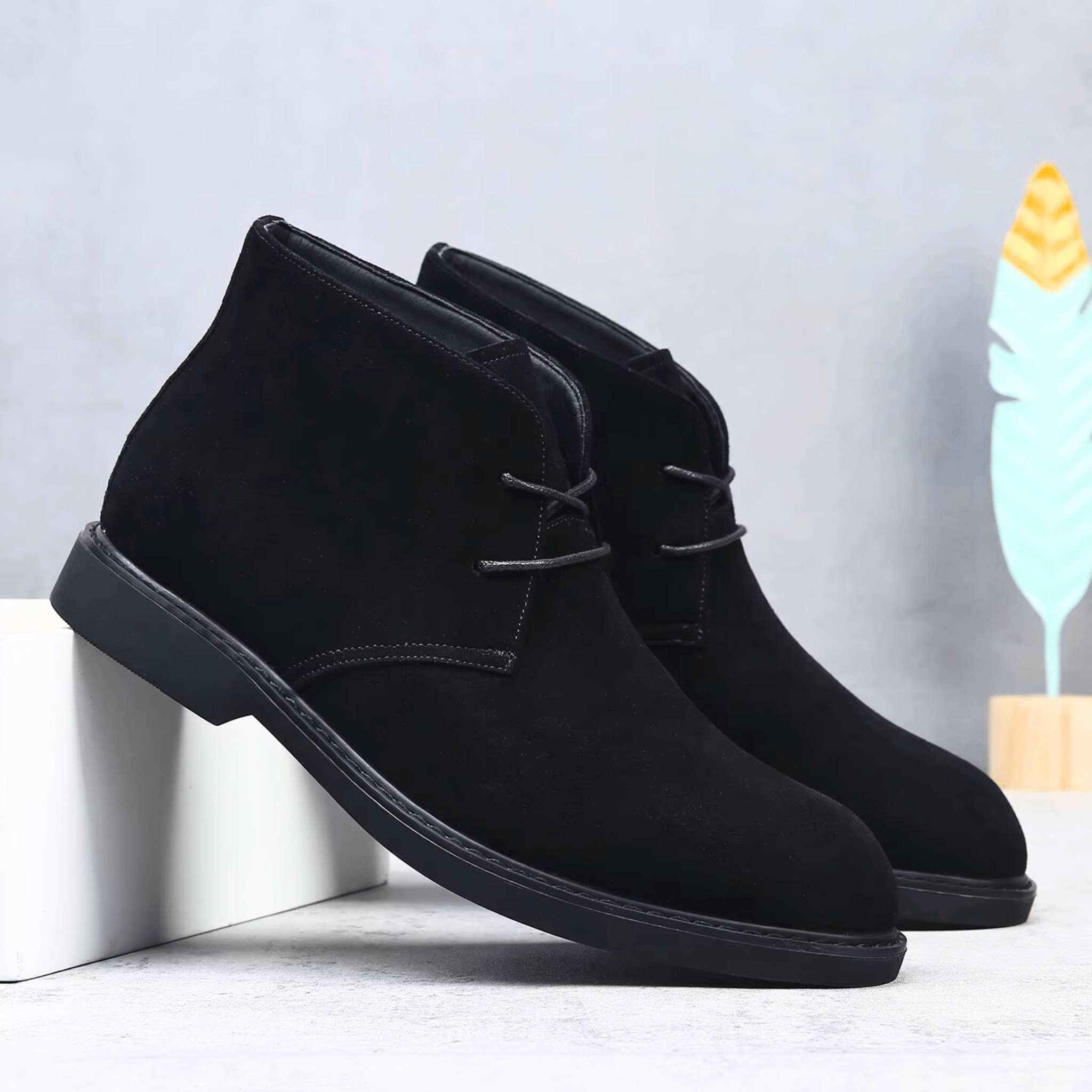 Black suede-look desert boots with a plain toe, two-eyelet lacing, and a low stacked heel on a clean, matte surface.