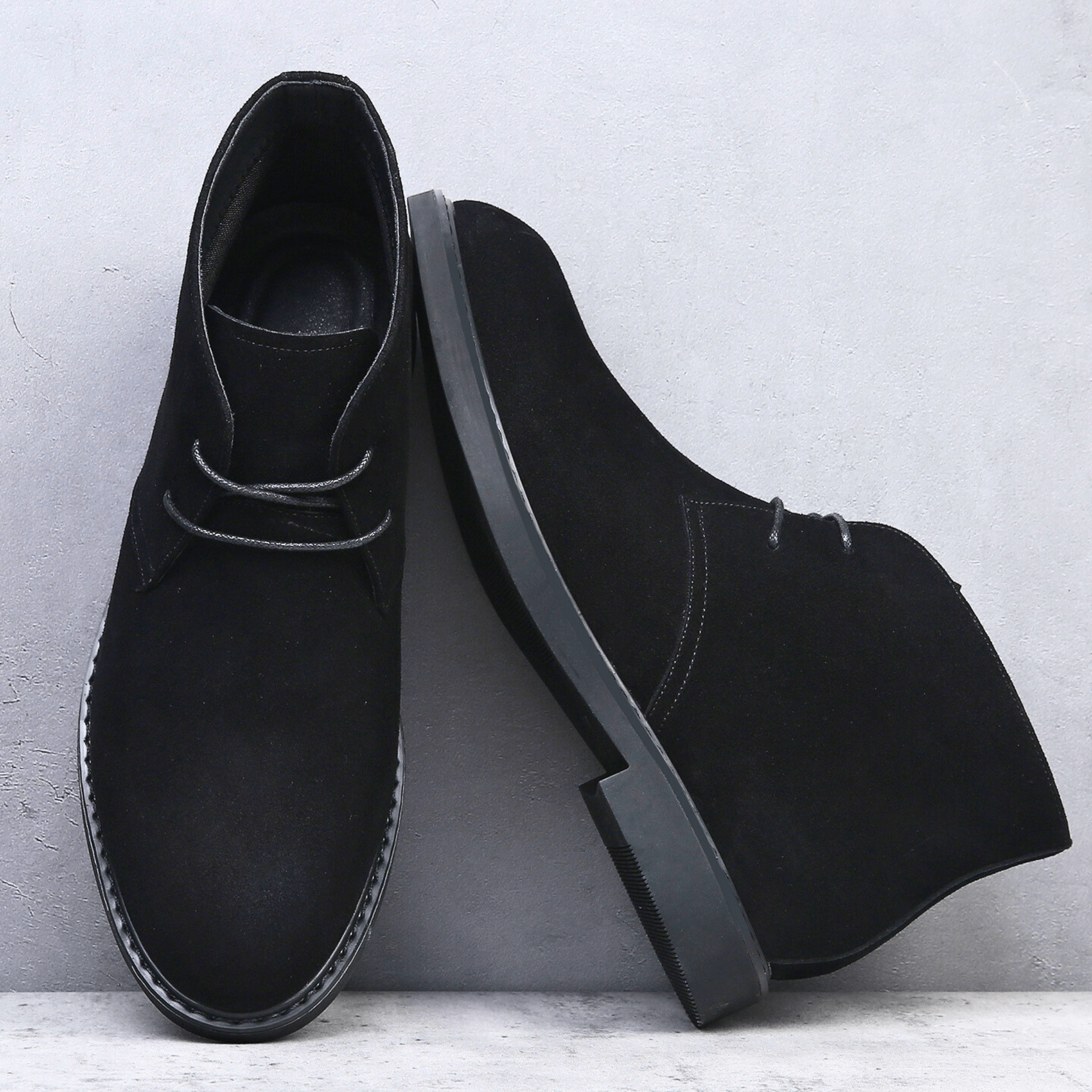 Black suede-look desert boots with a plain toe, two-eyelet lacing, and a low stacked heel against a grey background.