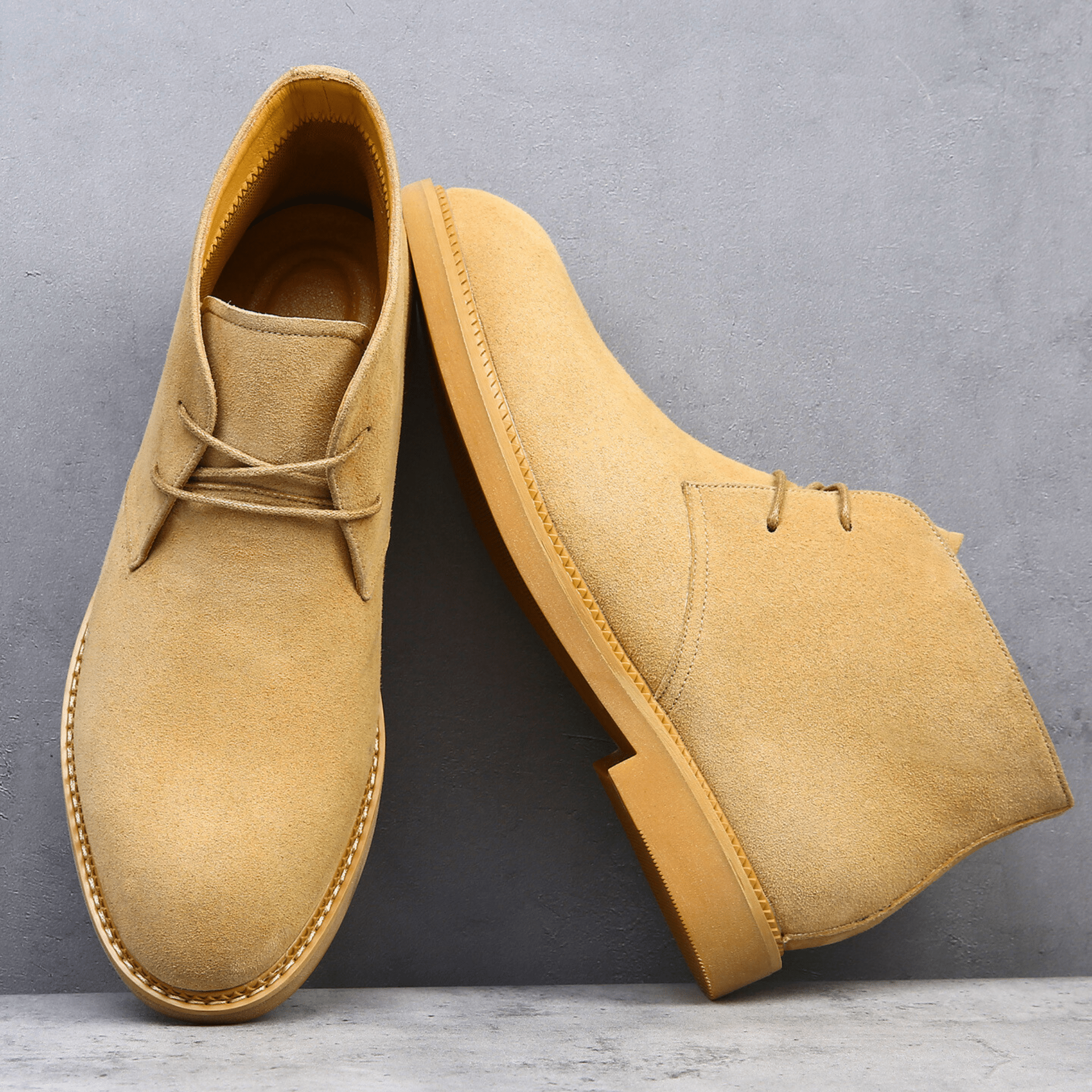 Tan suede-look desert boots with a plain toe, two-eyelet lacing, and a low stacked heel on a grey textured surface.