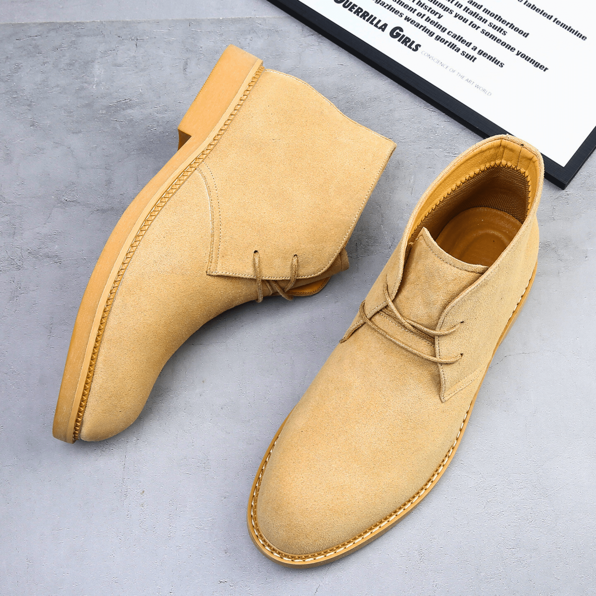 Tan suede-look desert boots with a plain toe, two-eyelet lacing, and a low stacked heel on a grey surface.