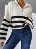 Cropped white chunky ribbed knit sweater with black stripes, half-zip collar, and flared sleeves worn with blue jeans.