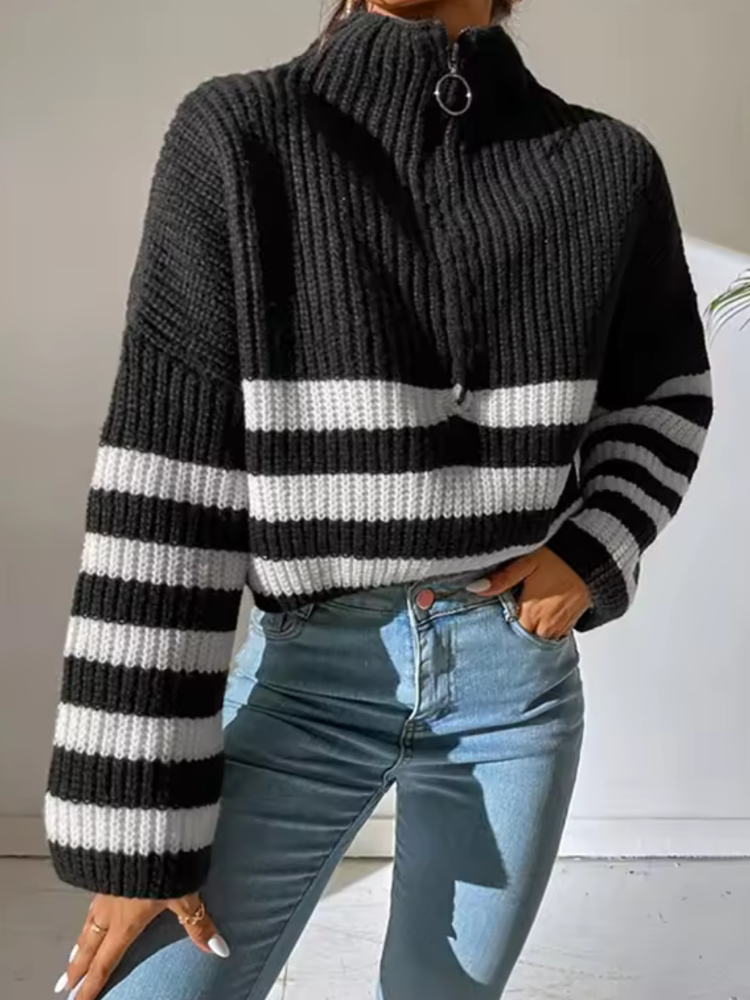 Black and white chunky ribbed knit sweater with a half-zip, folded collar, and flared sleeves, worn with blue jeans.