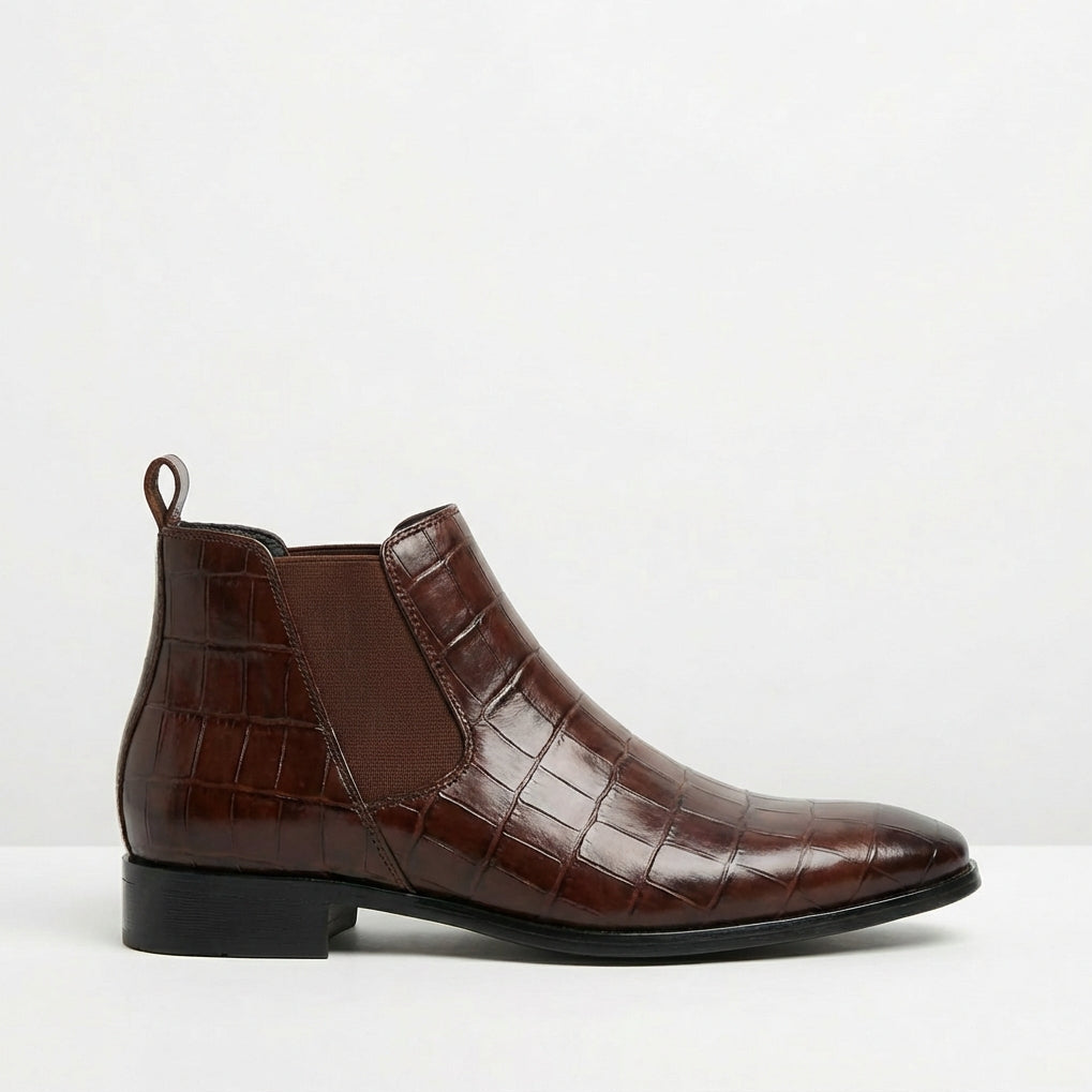 Dark brown croc-embossed Chelsea boots with a pointed toe, slim sole, and elastic side gore on a white background.