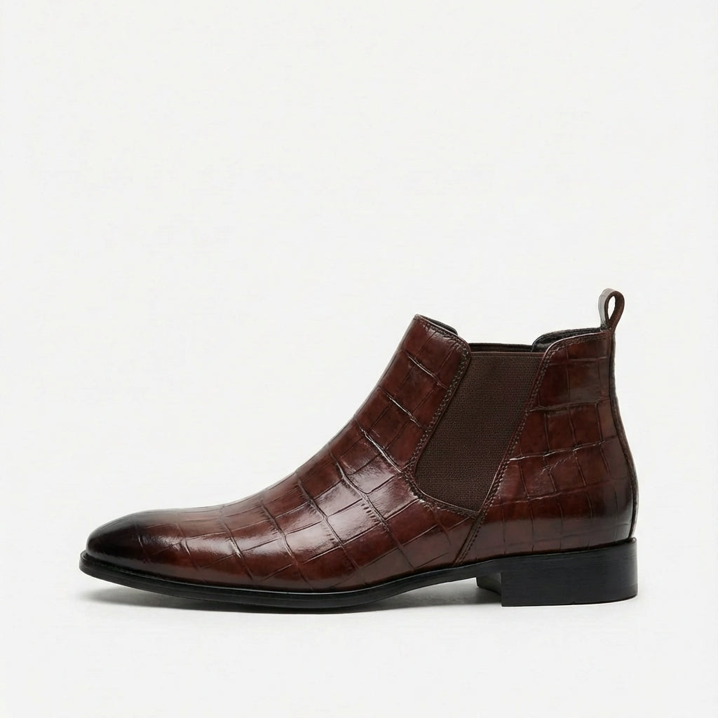 Dark brown croc-embossed Chelsea boots with a pointed toe, slim sole, and elastic side gore on a white background.