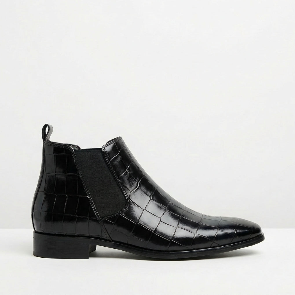 Black croc-embossed Chelsea boots featuring a sleek pointed toe, slim outsole, and elastic side gore on a white background.