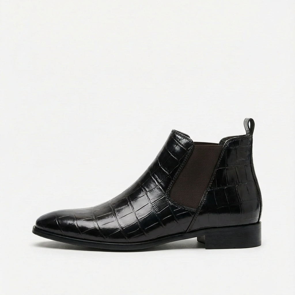 Black croc-embossed Chelsea boots with a pointed toe, slim outsole, and elastic side gore on a white background.