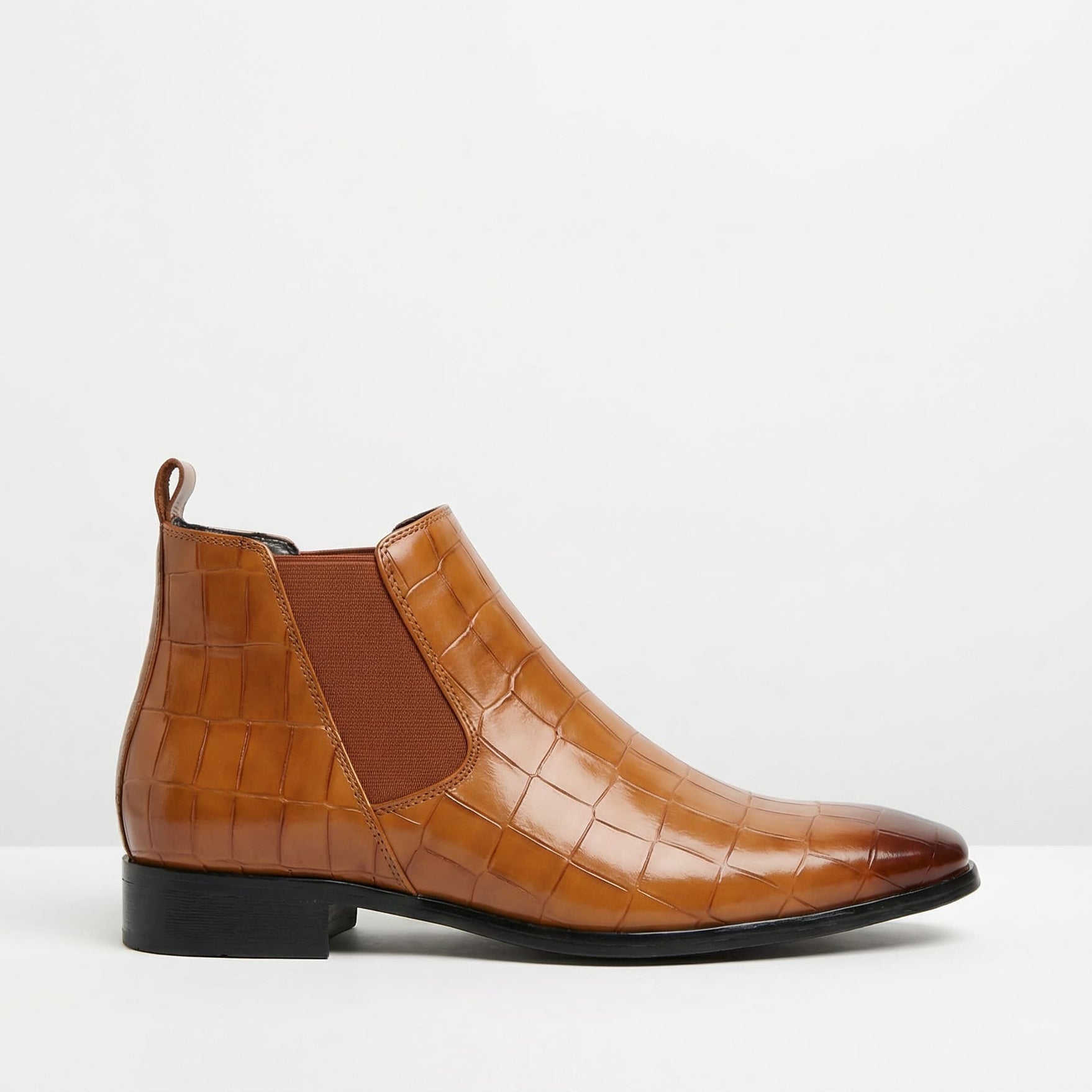 Tan croc-embossed Chelsea boots featuring a pointed toe, slim black outsole, and elastic side gore on a white background.