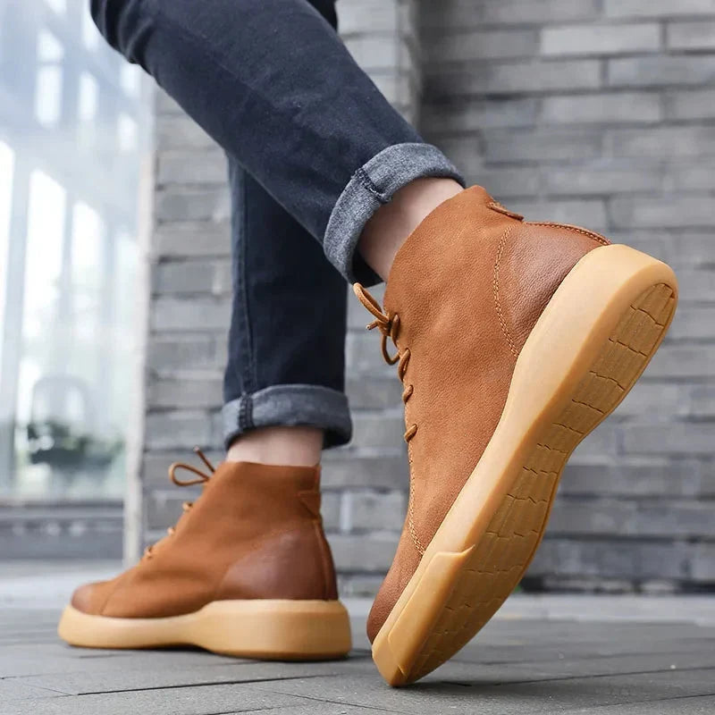 Tan smooth leather chukka boots with a chunky rubber sole, rounded toe, and lace-up closure worn with dark cuffed jeans.