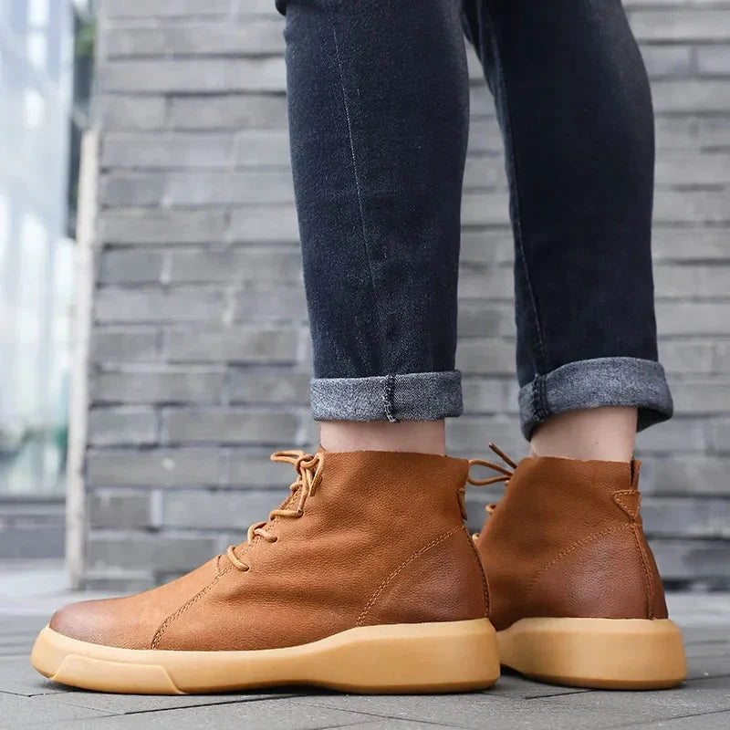 Tan leather chukka boots with a chunky rubber sole, rounded toe, and lace-up closure worn with cuffed dark denim jeans.