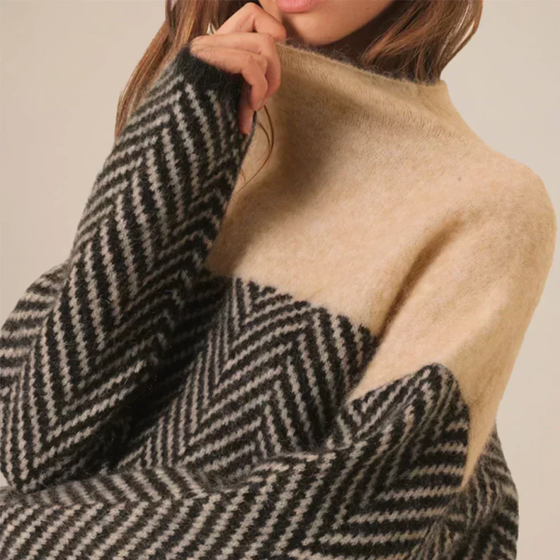 Close-up of a beige and gray color-block turtleneck sweater highlighting the soft knit texture, high collar, and herringbone pattern.