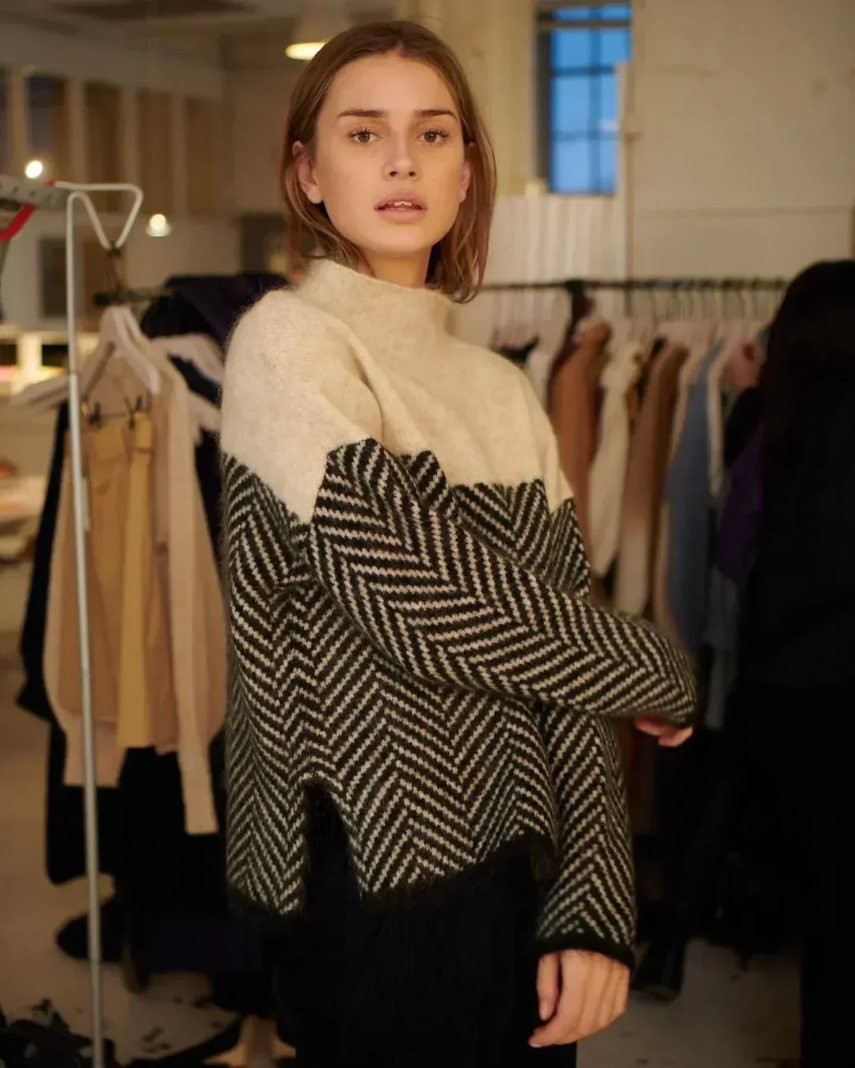 Beige and gray color-block turtleneck sweater with a herringbone knit pattern, worn in a casual indoor setting with a relaxed oversized fit.