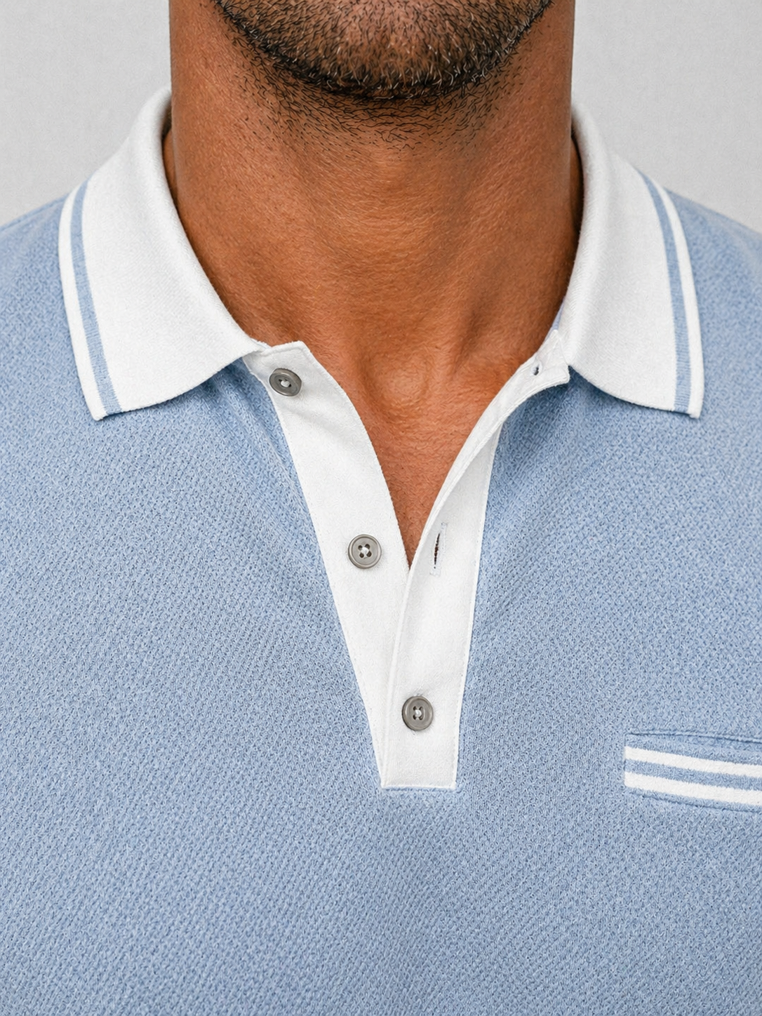 Light blue knit long-sleeve polo with a white contrast collar, button placket, and subtle chest pocket detail.