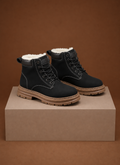 Black ankle boots with white fur lining, contrast stitching, lace-up metal eyelets, and a thick tan lug sole.