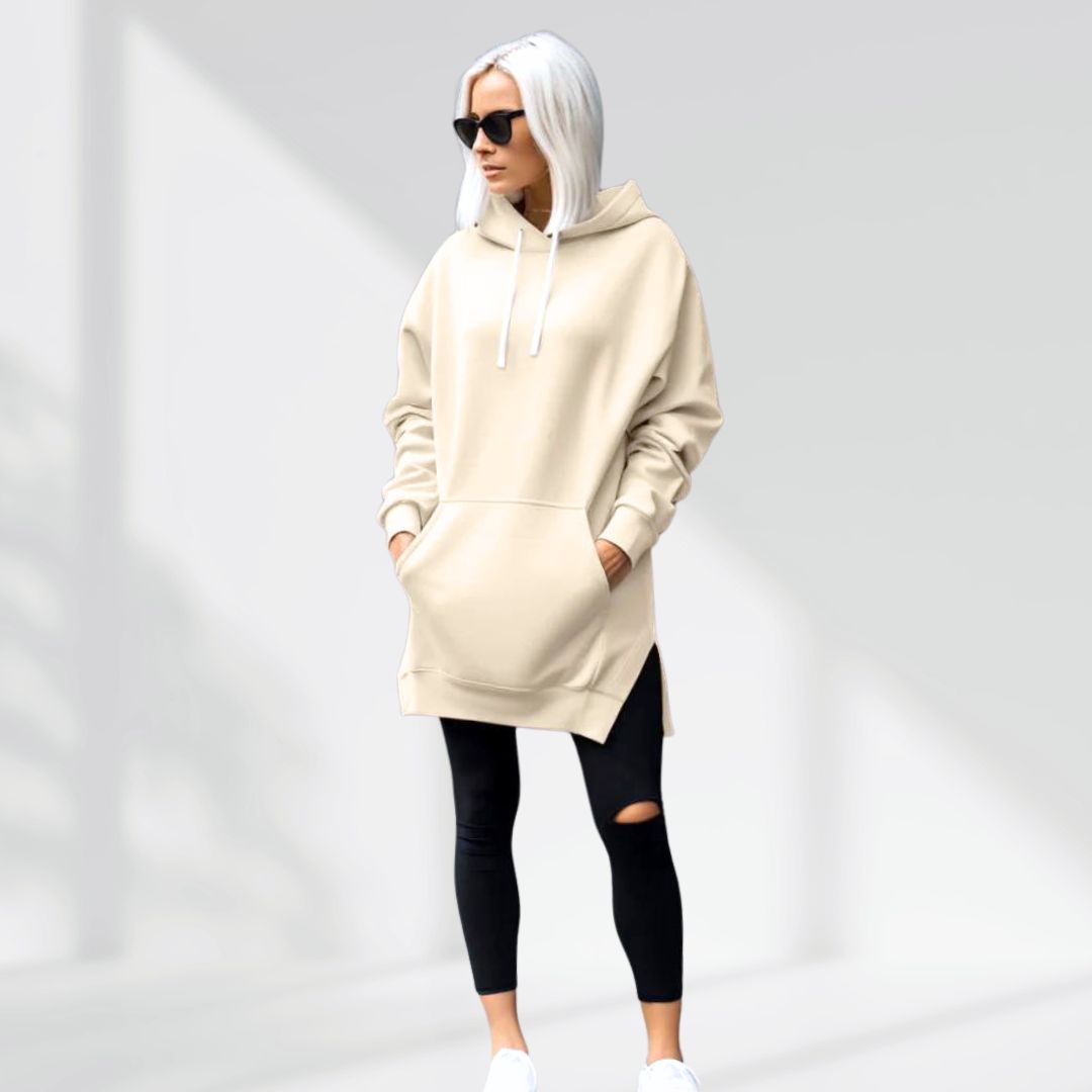 Oversized cream brushed cotton hoodie with a drawstring hood, longline hem, and side slits worn over black leggings.