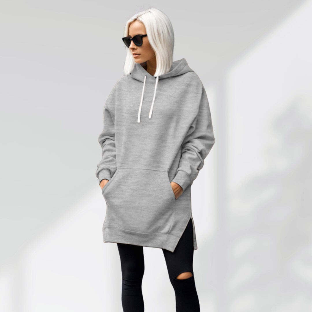 Oversized grey brushed cotton hoodie with a longline silhouette, drawstring hood, and side-slit hem worn over leggings.