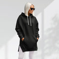 Oversized black brushed cotton hoodie with a longline hem, side slits, and a drawstring hood worn over white leggings.