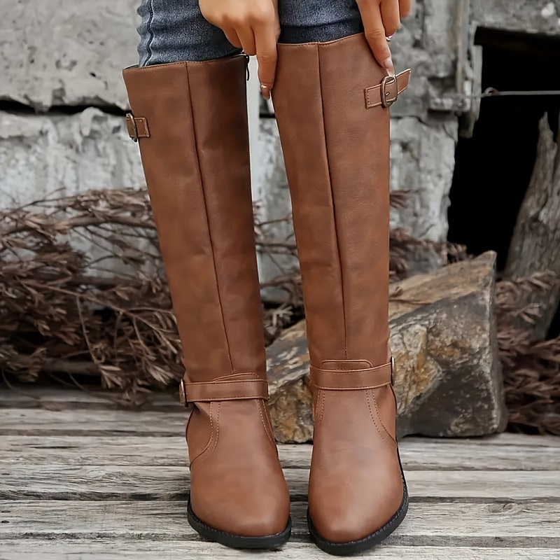 Brown knee-high boots with structured shafts, antique buckle straps at the ankle and cuff, and a stacked block heel.