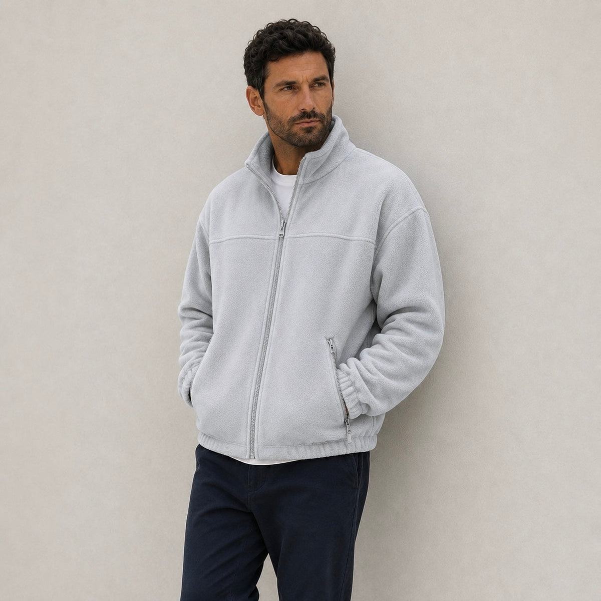 A man wearing a light gray full-zip fleece jacket with a stand-up collar, paired with dark pants.