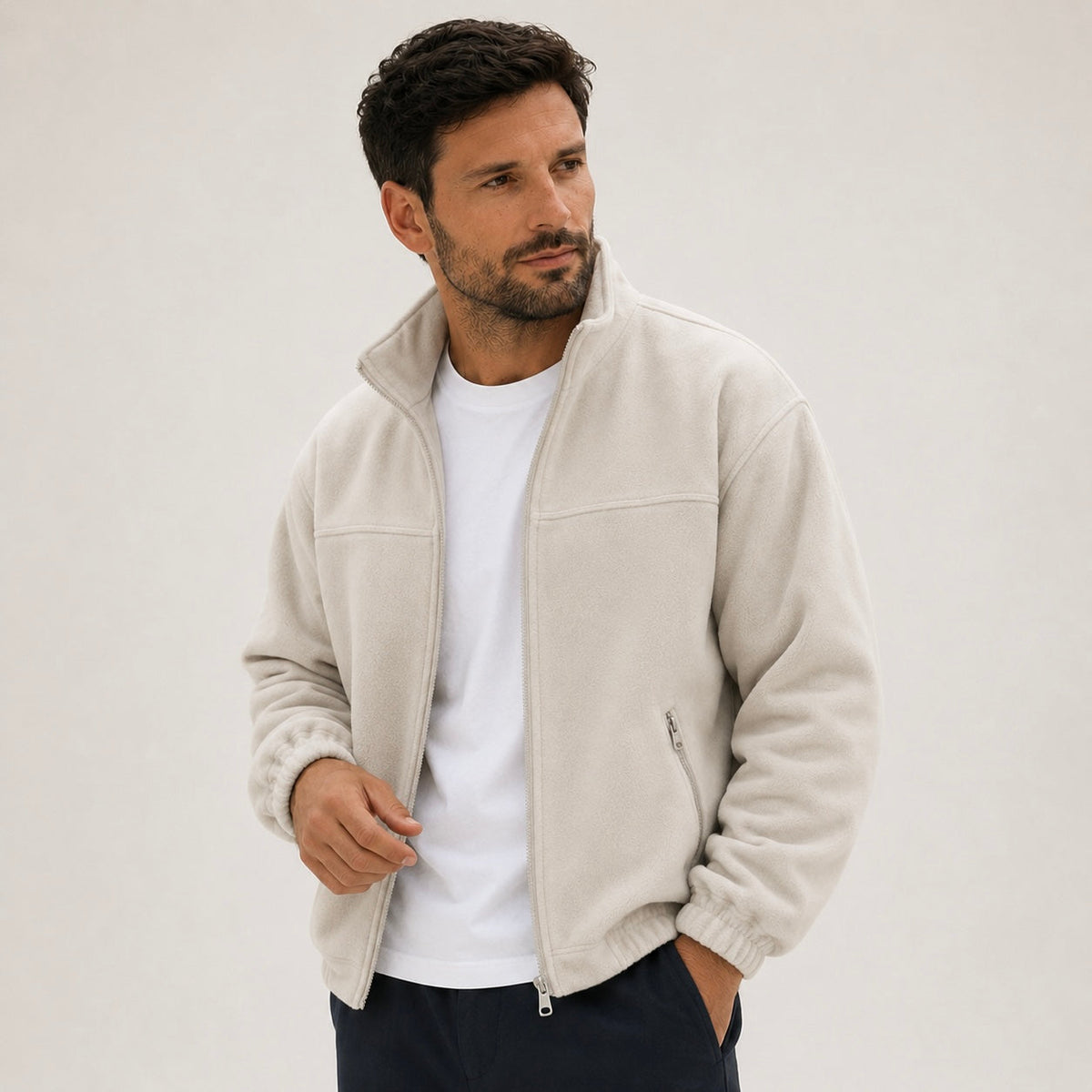 A man wearing a cream full-zip fleece jacket with a high collar open over a white t-shirt.