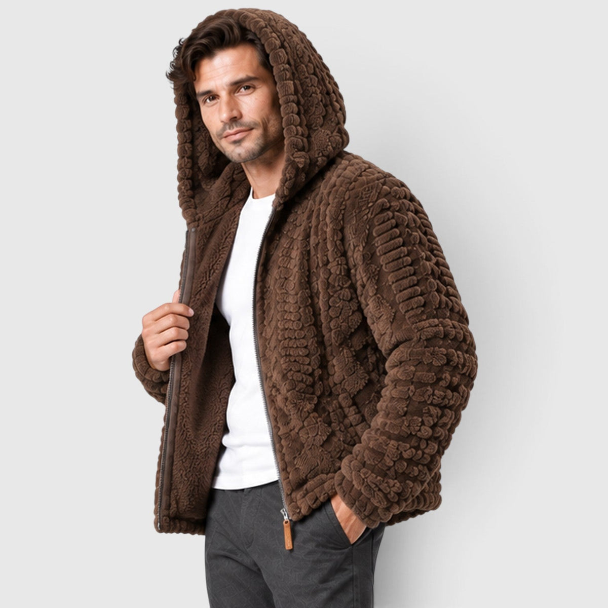 A man wearing a dark brown cable-textured hooded fleece jacket with the hood up, styled open over a white t-shirt and dark trousers