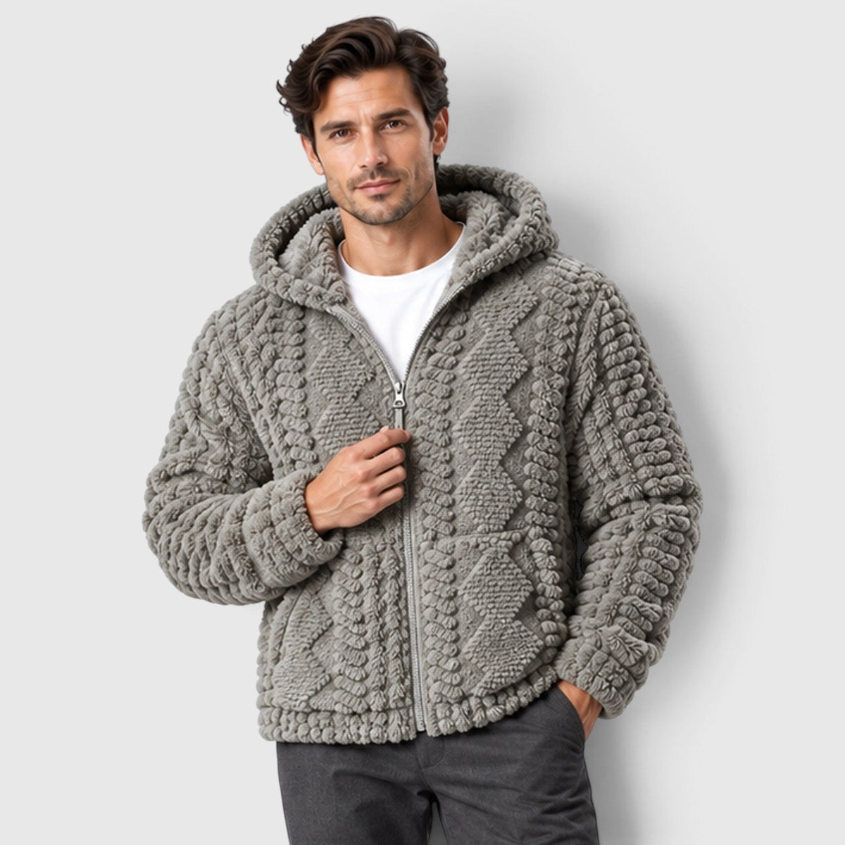A man wearing a light gray hooded cable-textured fleece jacket zipped up over a white t-shirt and dark trousers.