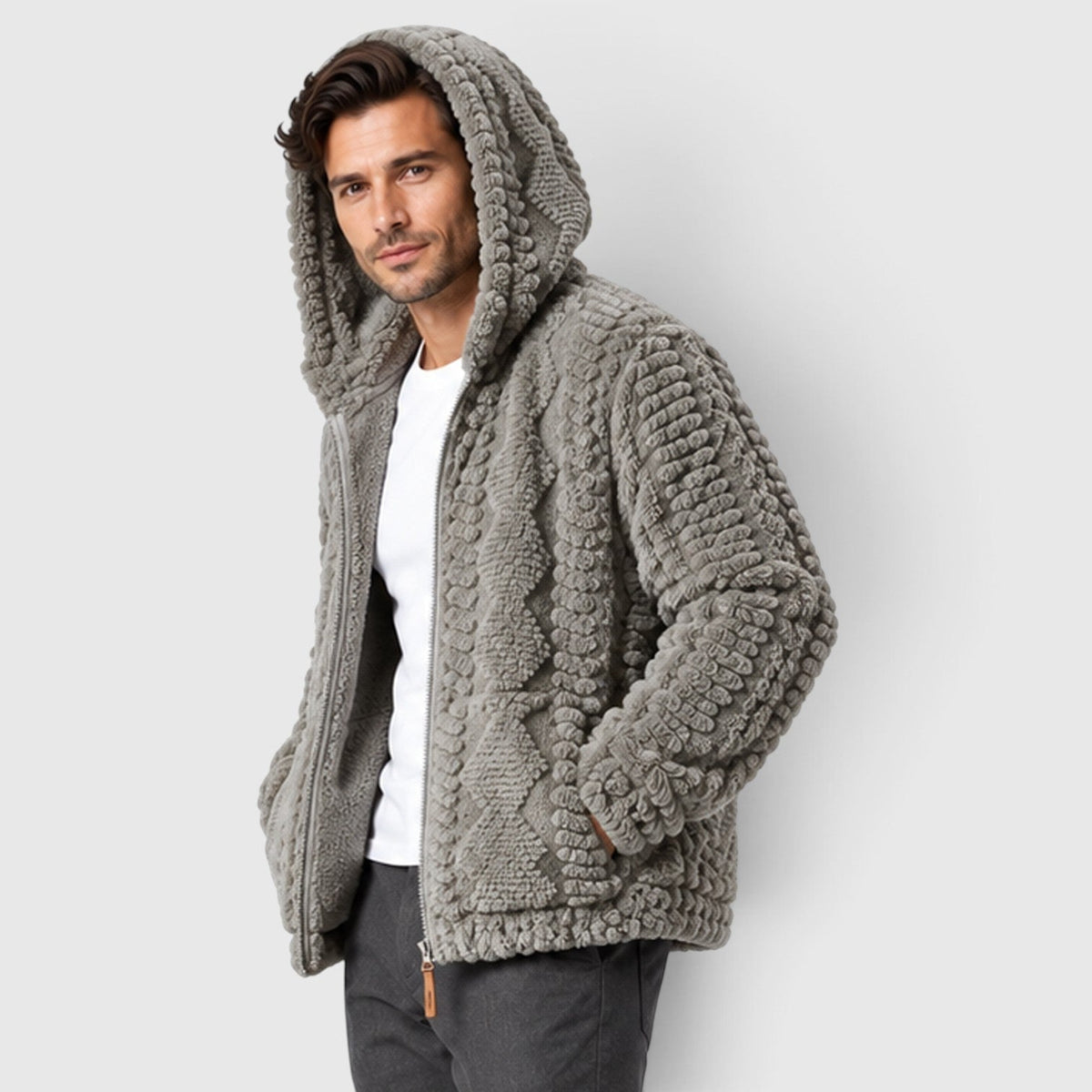 A man wearing a light gray hooded cable-knit fleece jacket with the hood up, hands in pockets.