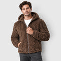 A dark-haired man wearing a dark brown hooded fleece jacket with an embossed cable-texture pattern and full front zipper, styled over a white t-shirt and dark trousers.