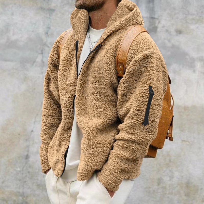 A man wearing a camel hooded teddy fleece zip jacket featuring a sleeve zippered pocket, styled with a white top and leather backpack.