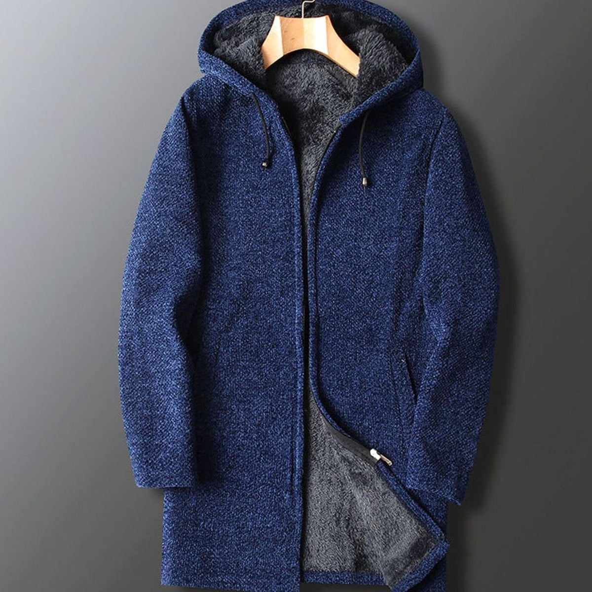 A men's longline hooded coat in navy blue with a textured knit shell and soft dark fleece lining, displayed on a hanger.