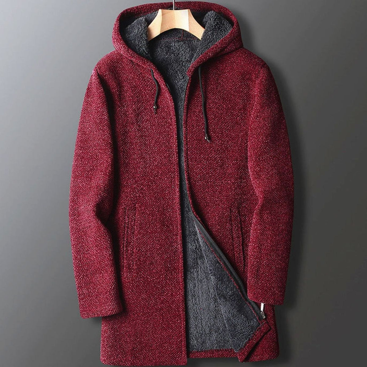 A men's burgundy wine-red longline hooded coat featuring a textured outer fabric and plush dark fleece lining, shown hanging on a wooden hanger.