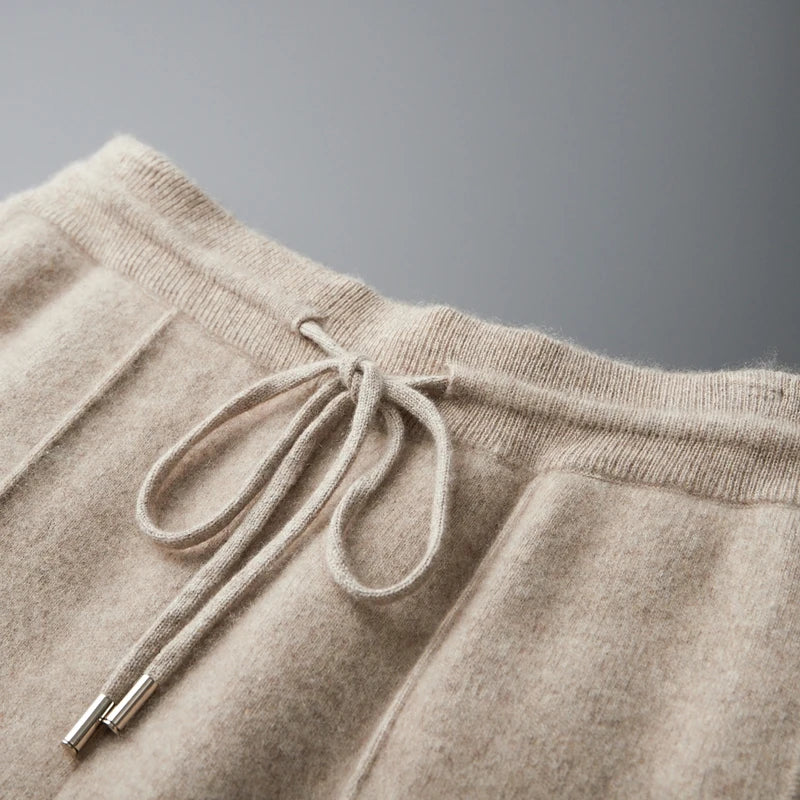 Beige merino wool trousers featuring a soft-touch knit texture, an elastic drawstring waist, and metal-tipped cord ends.