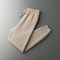 Beige merino wool trousers with a drawstring waist, straight-leg silhouette, and tapered ribbed ankles.
