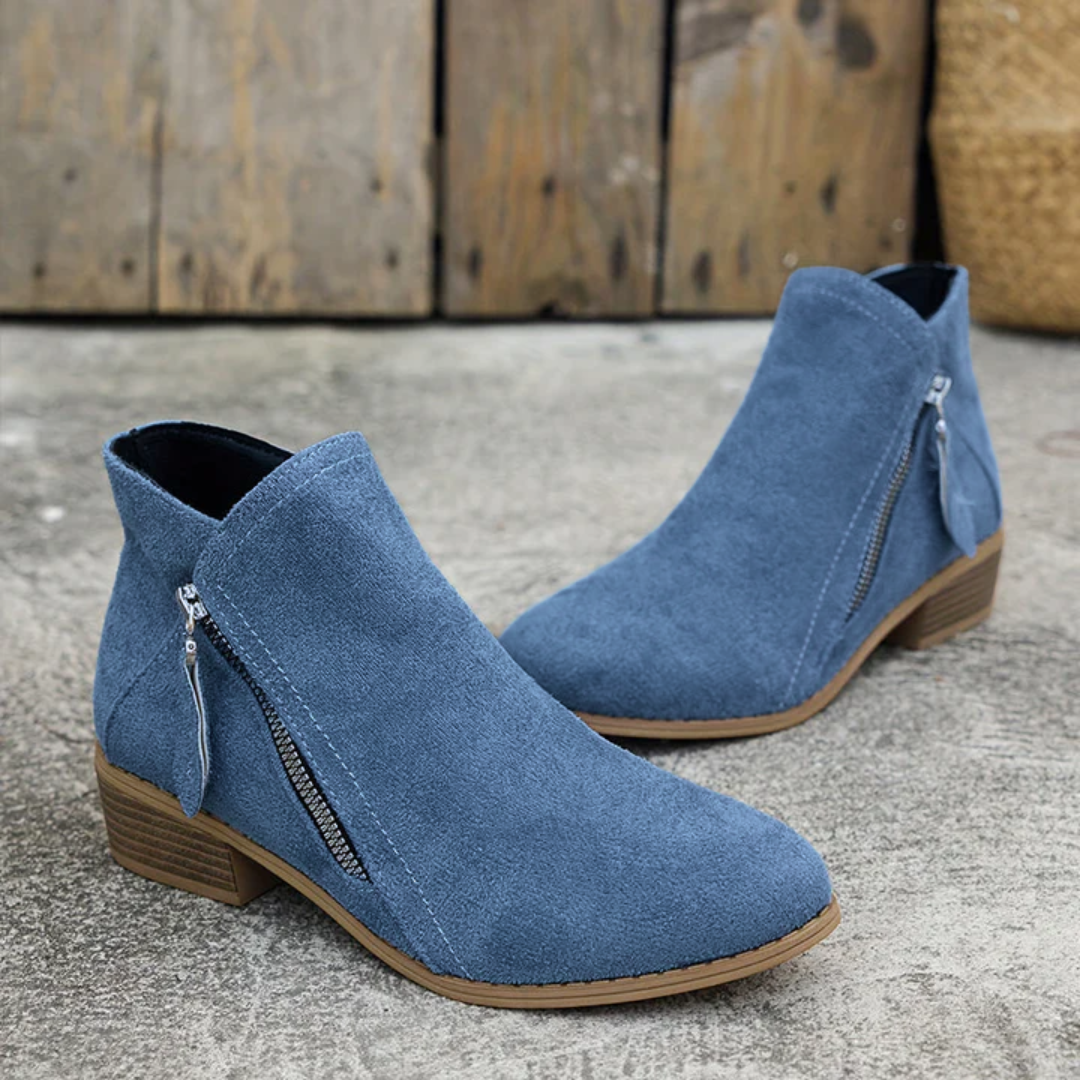 Blue brushed suede low-cut booties with an almond toe, angled side zipper, and a stacked block heel on a concrete surface.