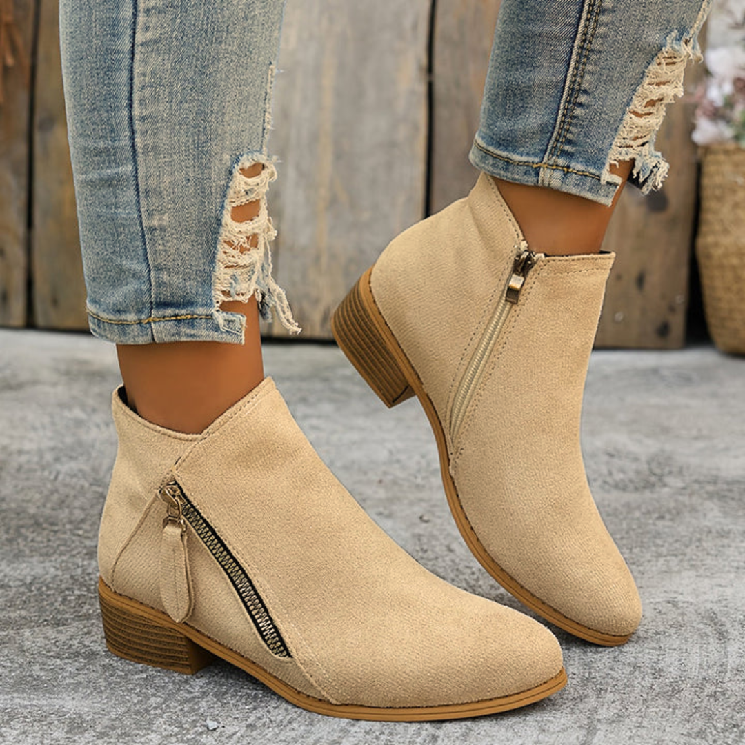 Beige brushed-finish ankle booties with an angled side zip and low block heel, styled with distressed blue jeans.