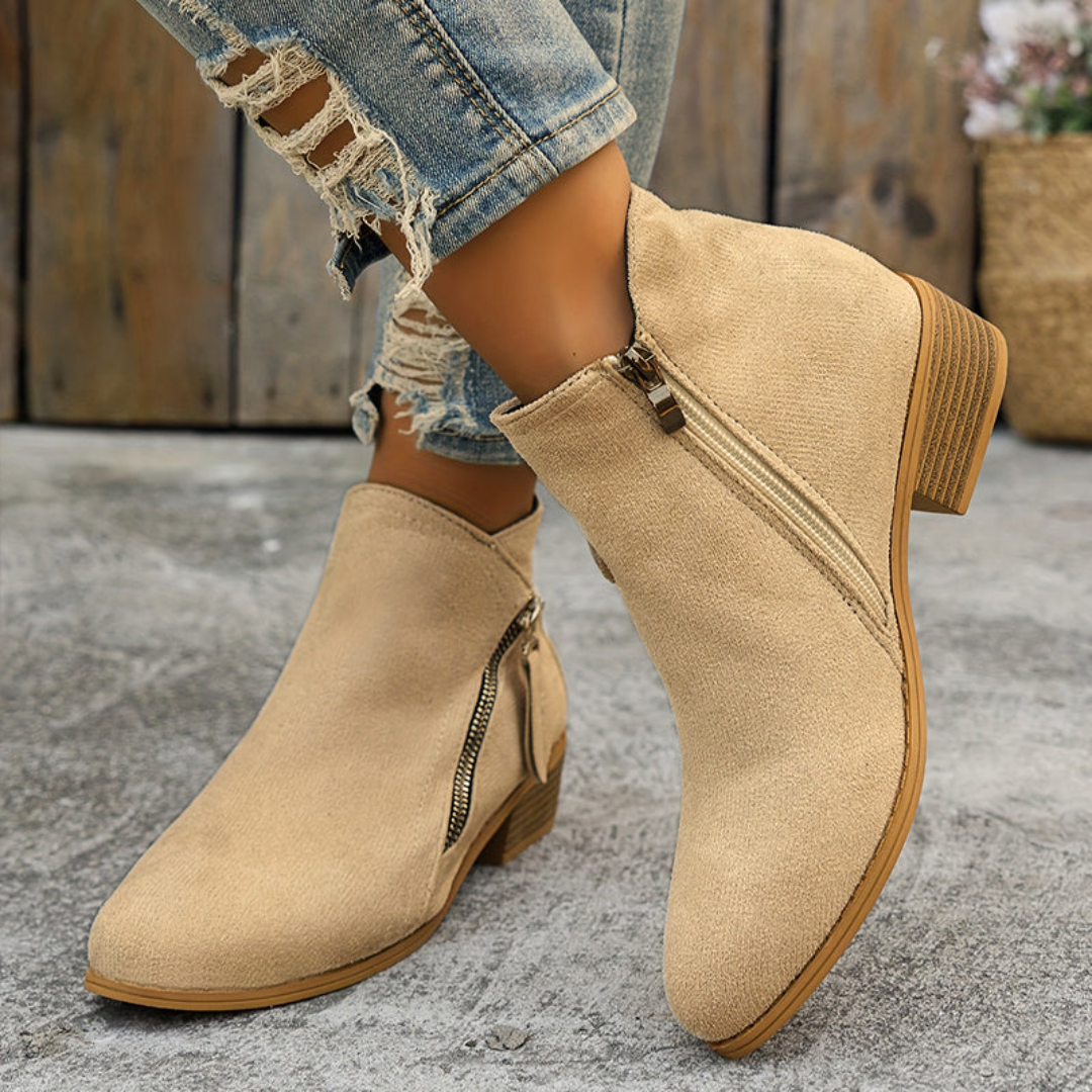 Beige brushed-finish block heel booties with an angled side zipper and almond toe, styled with distressed denim.