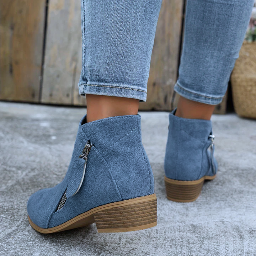 Blue brushed-finish low-cut booties with an angled side zip and stacked block heel, worn with light-wash denim jeans.