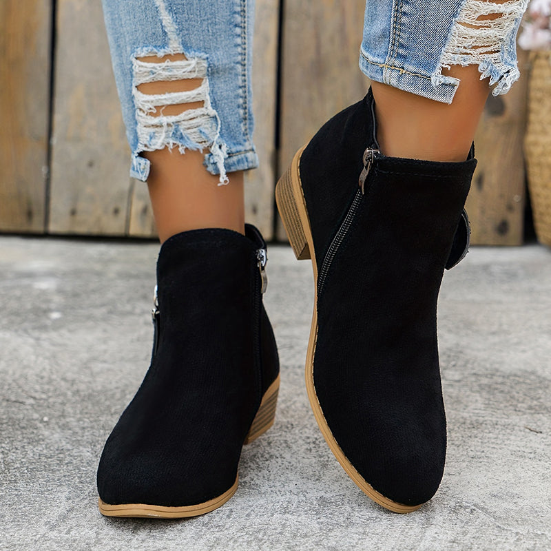 Black brushed-finish almond toe booties with low block heels and angled side zips, worn with distressed blue jeans.