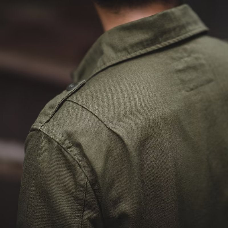 Close-up view focusing on the back shoulder yoke, spread collar construction, and shoulder epaulet seam detail of the olive green utility jacket.
