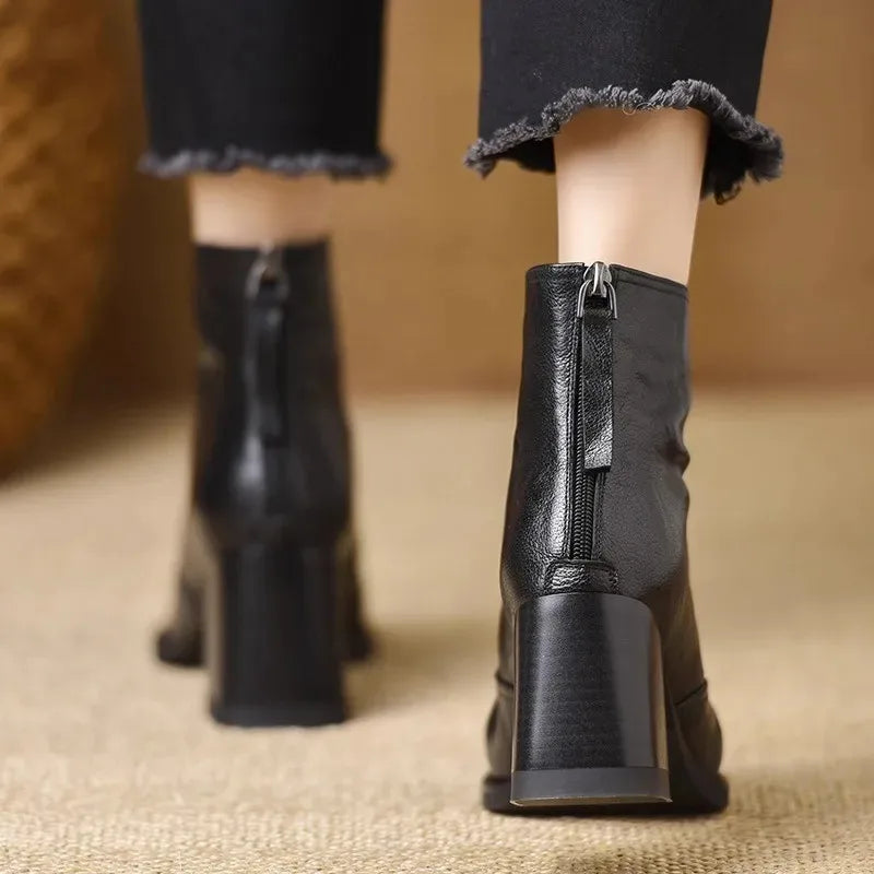Black leather ankle boots featuring a tall block heel, rear zip closure, and a structured, modern silhouette.