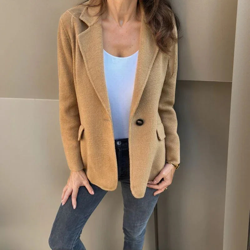 Camel wool single-button blazer with notched lapels and welt pockets, worn over a white tank and dark denim jeans.