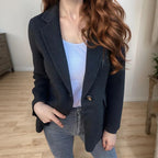 Charcoal wool single-button blazer with a notched lapel and structured silhouette worn over a white top and grey jeans.