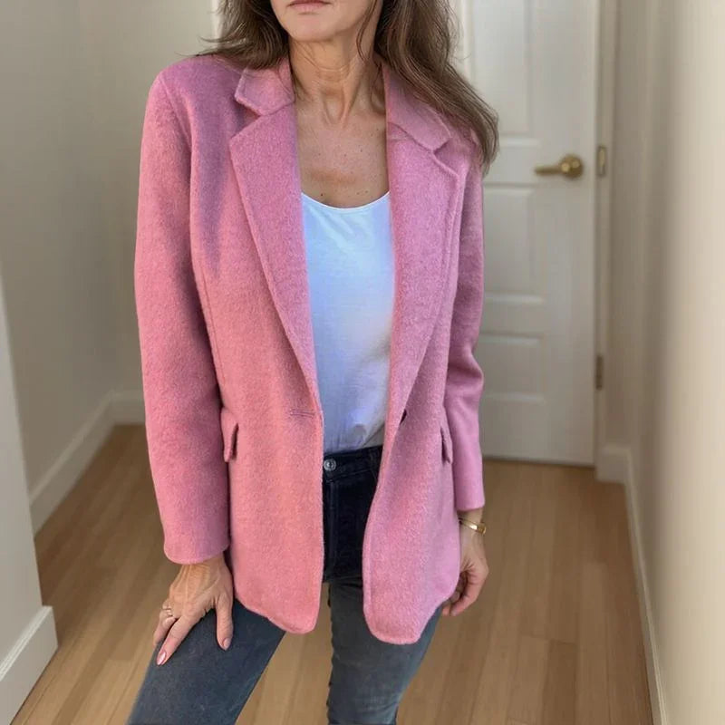 Structured pink wool blazer with a single-button closure, notched lapels, and welt pockets worn over dark denim.