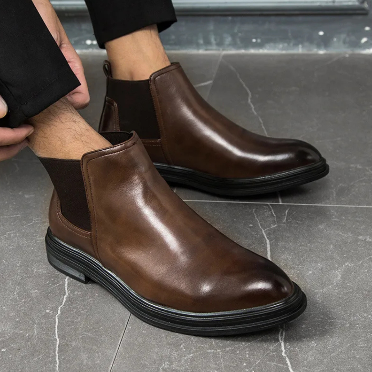 Smooth brown leather Chelsea boots with elastic side gores and a chunky black lug sole, worn with tailored trousers.