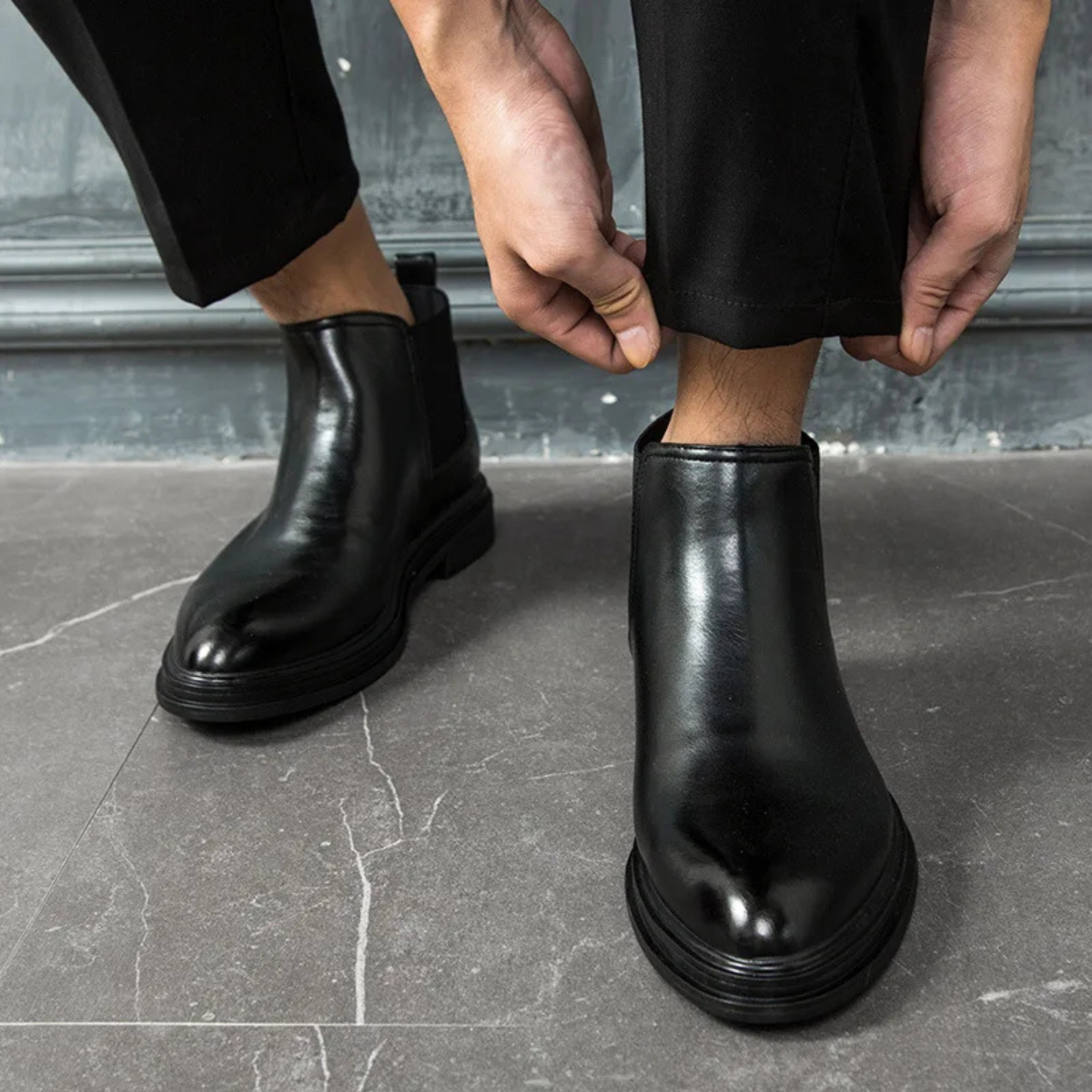 Black smooth leather Chelsea boots with a chunky lug sole and elastic side panels, worn with tailored trousers.