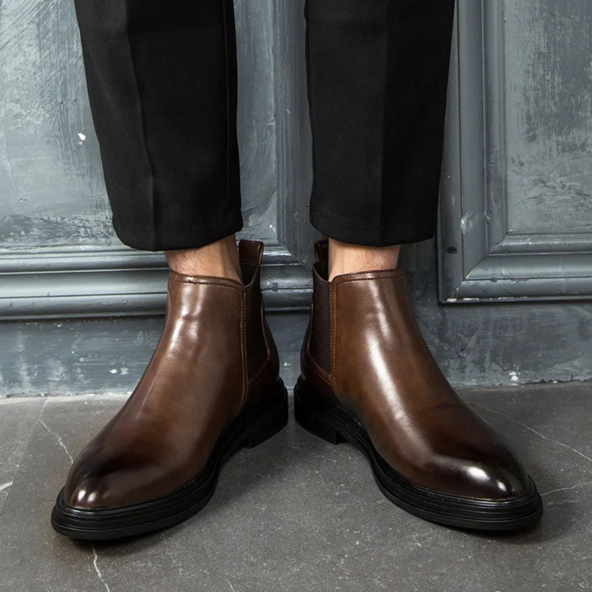 Brown leather Chelsea boots with a round toe, elastic side gores, and a chunky black lug sole worn with black trousers.