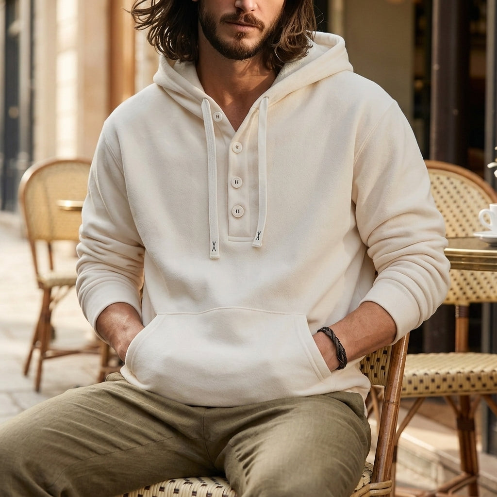 Cream oversized henley hoodie worn by a male model, shown seated with the button placket and kangaroo pocket visible.