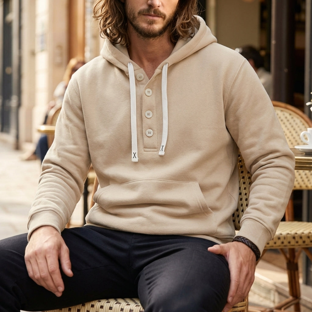 Beige oversized henley hoodie worn by a male model, shown seated with the button placket and kangaroo pocket visible.