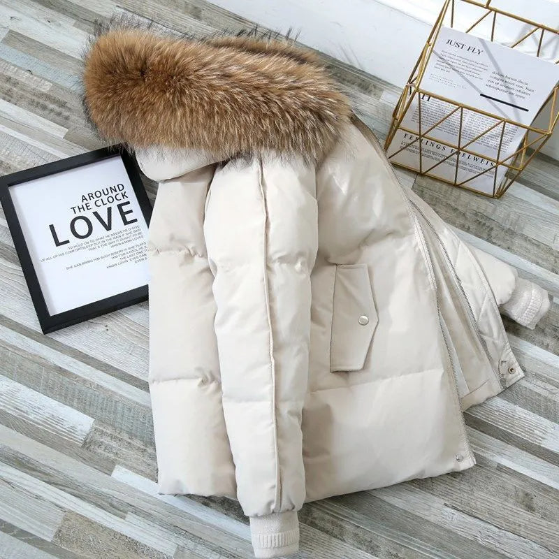 Oversized white puffer jacket with a plush-trim hood, quilted snap placket, and ribbed knit cuffs on a wooden surface.