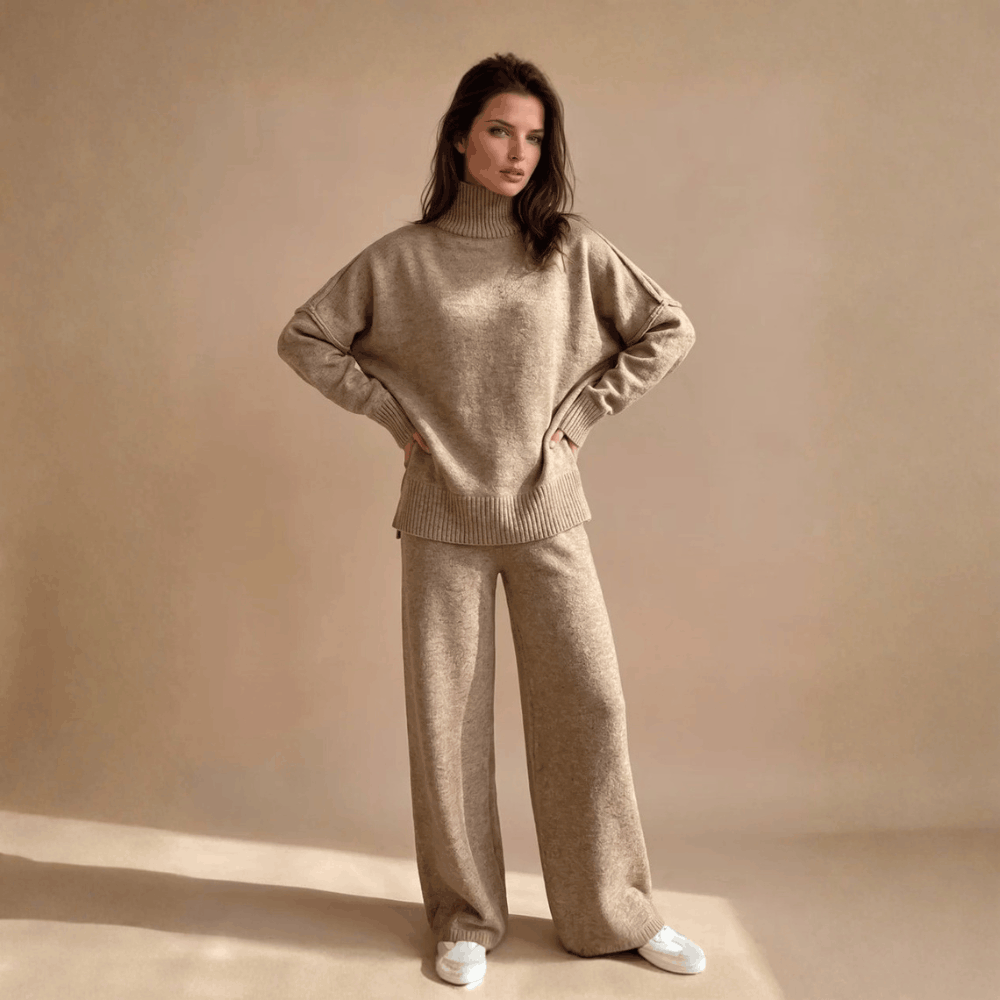 Full-length front view of a model posing with hands on her waist wearing the beige oversized turtleneck sweater and matching knit wide-leg pants.